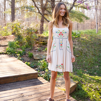 Woman wearing a floral embroidered dress standing on a wooden platform in a garden.