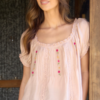 Woman wearing a light pink blouse with floral embroidery against a blurred background